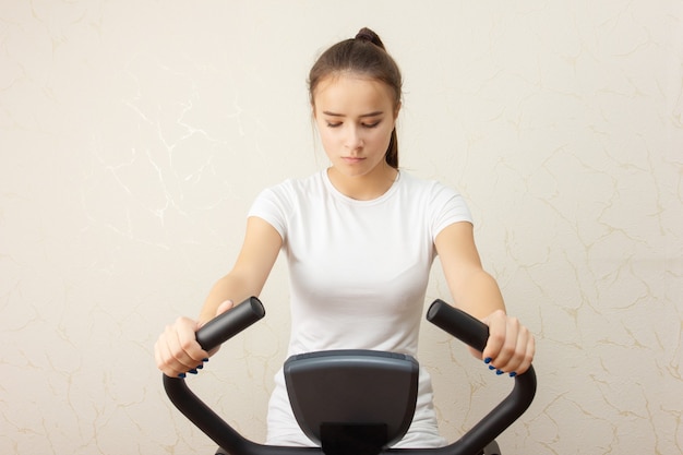 若い女の子はジムでエアロバイクに従事しています