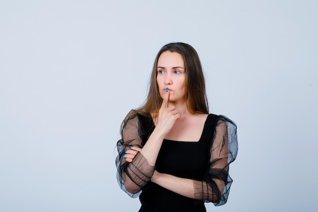 Young girl is looking away by putting forefinge ron lips on white background