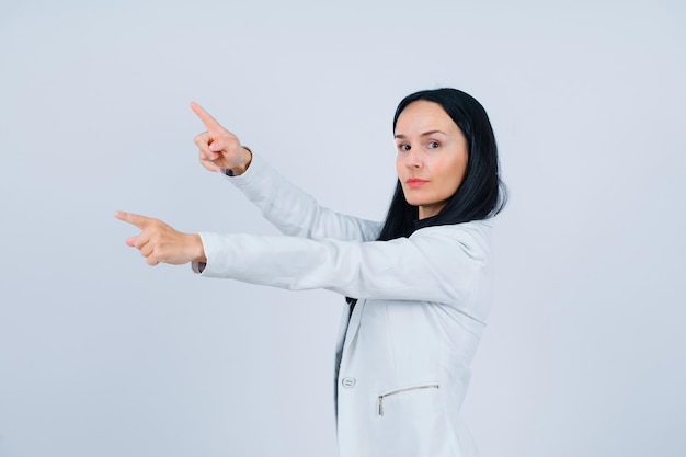 Young girl is looking at camera by pointing left with forefingers on white background