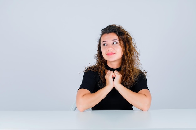 La ragazza sta guardando a sinistra tenendo insieme i pugni sul petto su sfondo bianco