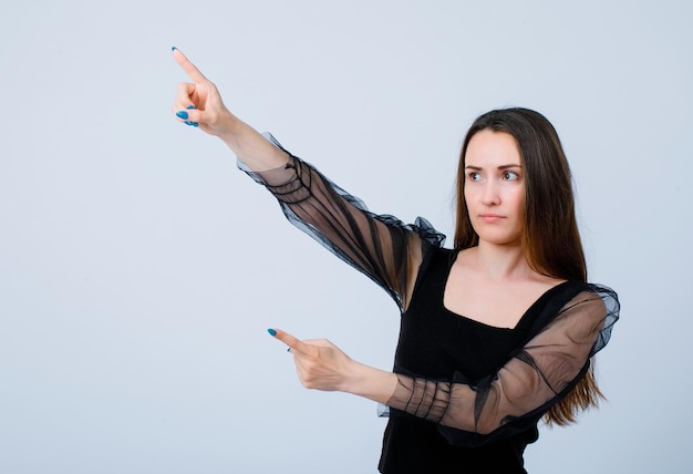 Young girl is looking left up and pointing there with forefingers on white background