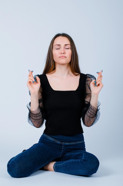 Young girl is meditating by raising up crossed fingers on white background