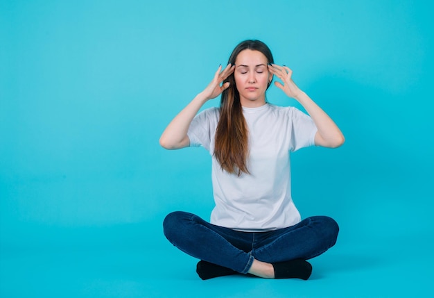 Young girl is meditating by sitting on floor on blue background