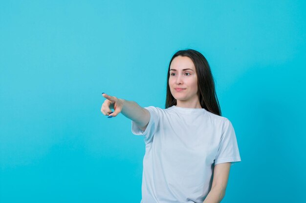 Young girl is pointing away with forefinger on blue background