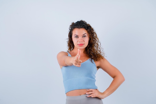 Young girl is pointing to camera with forefinger on white background