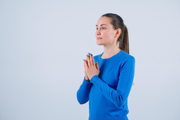 Молодая девушка молится, взявшись за руки на белом фоне