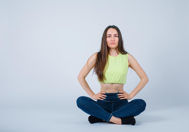 Young girl is putting hands on waist by sitting on floor on white background