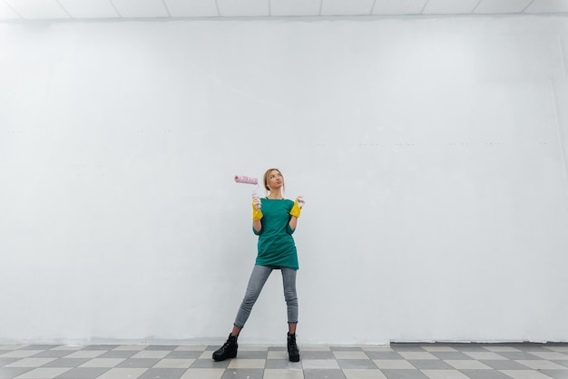 A young girl is repairing a krusty white wall and smiling with a pink roller in her hands