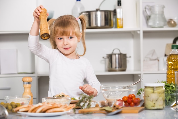 Young girl is salting the salad in time cooking in the kitchen