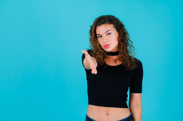 Young girl is showing hi gesture by extending hand to camera on blue background