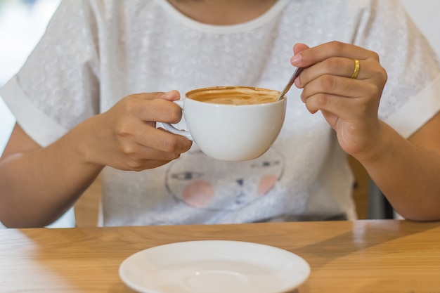 Молодая девушка сидит и пьет кофе латте в кафе.