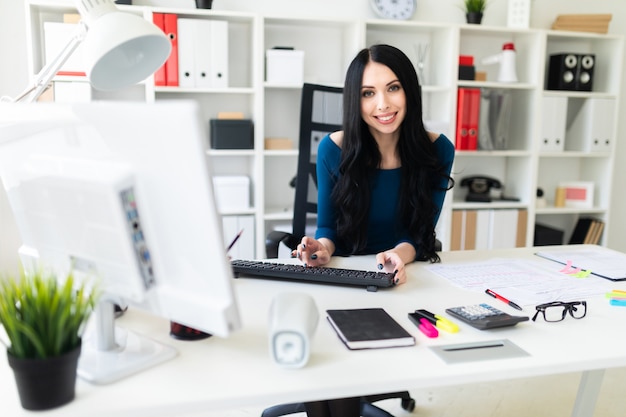 A young girl is sitting at the office at the table and typing text on the keyboard.