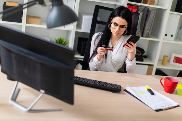 A young girl is sitting at the table, holding a bank card and phone