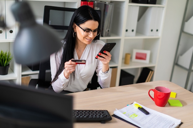 A young girl is sitting at the table, holding a bank card and phone.