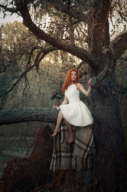 Молодая девушка сидит на дереве в лесу