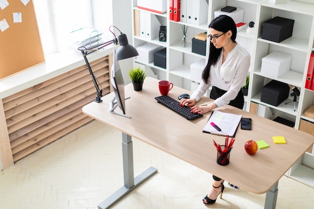 A young girl is standing near the table and typing text on the keyboard.