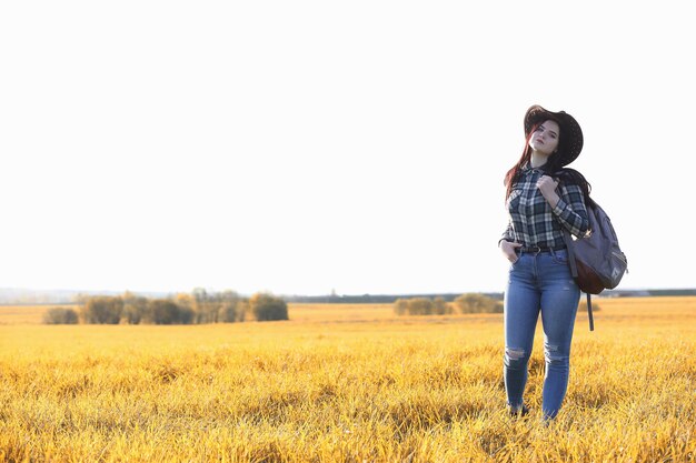 Photo a young girl is traveling around the city hitchhiking a beautiful young girl went on vacation a female student in a cowboy hat on the road in autumn