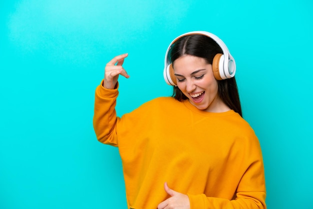 Young girl isolated on blue background listening music and doing guitar gesture