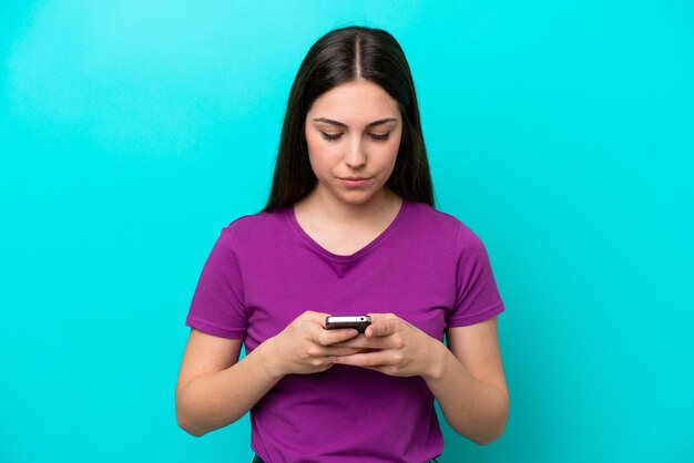 Молодая девушка изолирована на синем фоне с помощью мобильного телефона