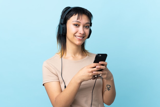 Young girl over isolated blue listening music with a mobile and looking front