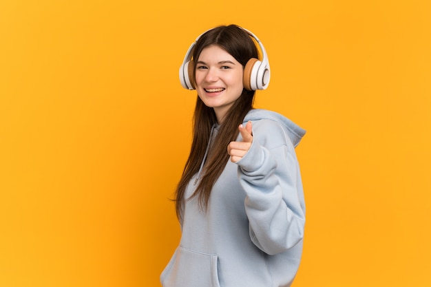 Young girl over isolated listening music and pointing to the front