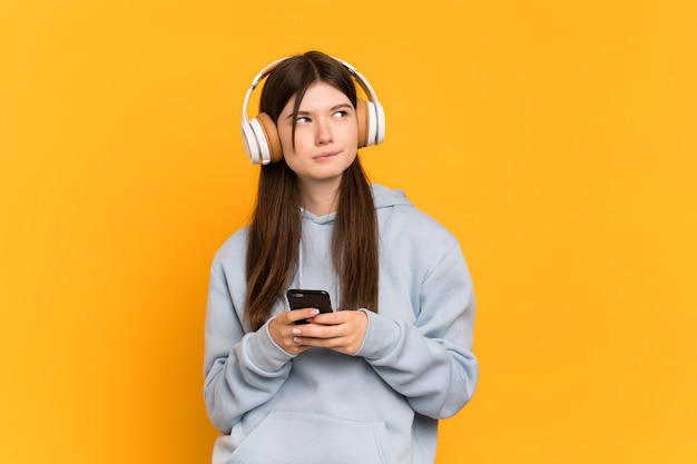 Young girl over isolated listening music with a mobile and thinking