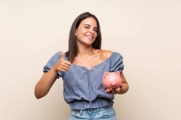 Young girl over isolated wall holding a big piggybank