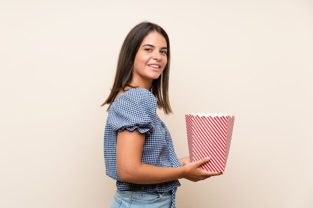 Young girl over isolated wall holding a bowl of popcorns