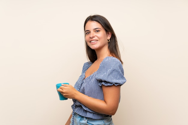 Young girl over isolated wall holding hot cup of coffee