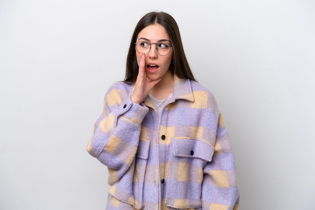 Young girl isolated on white background whispering something with surprise gesture while looking to the side