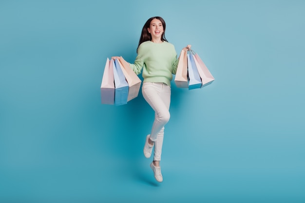 어린 소녀 점프는 파란색 배경에 고립 된 쇼핑백을 나른다