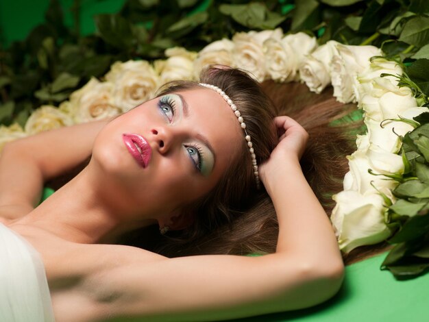 Young girl lay among the flowers of roses on a green background