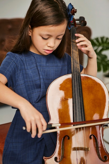 写真 家でチェロを弾く方法を学ぶ少女