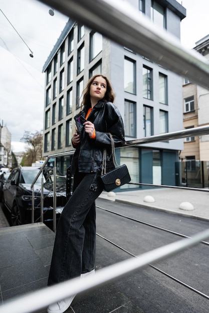 Young girl in leather jacket posed in urban city holding credit card with handbag and phone