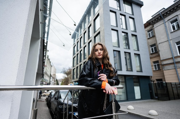 Young girl in leather jacket posed in urban city holding credit card with handbag and phone