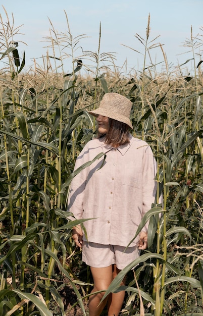 Una giovane ragazza con un vestito di lino e un cappello in una giornata di sole estivo si trova in un campo di mais amore per il viaggio e