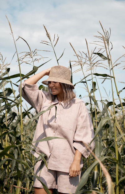 Young girl in a linen suit and a hat on a summer sunny day stands in a corn field love of travel and