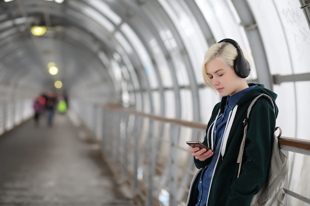 young girl listens to music in big headphones in the subway tunnel