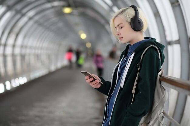 Молодая девушка слушает музыку в больших наушниках в туннеле метро