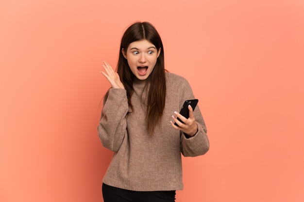 Young girl looking at the camera while using the mobile with surprised expression