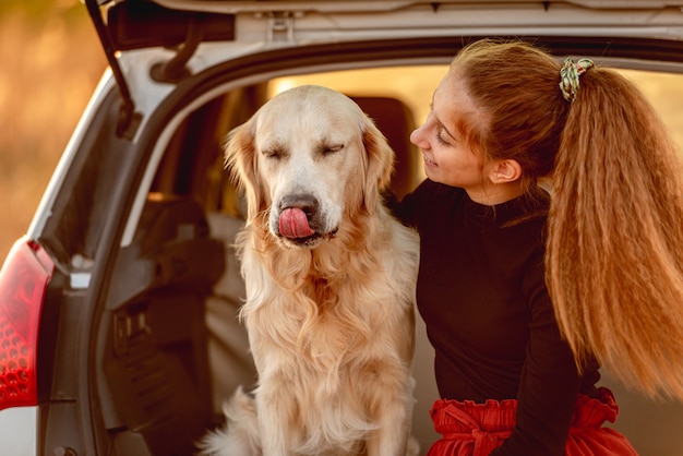 Young girl looking at golden retriever dog while sitting in open car trunk outdoors