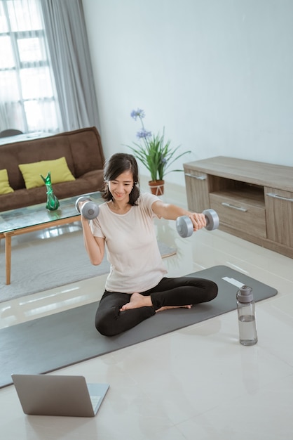 Young girl looking at laptop and doing exercises at home by her self