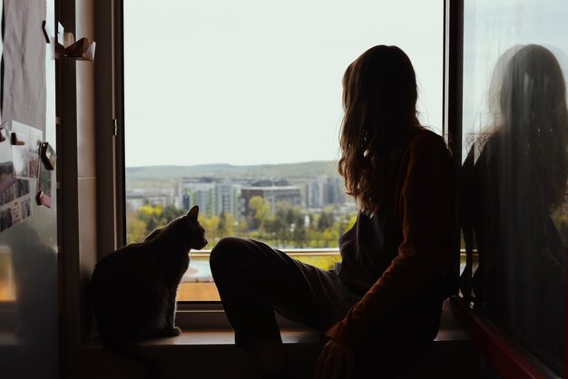 写真 猫と一緒に窓から外を見ている若い女の子