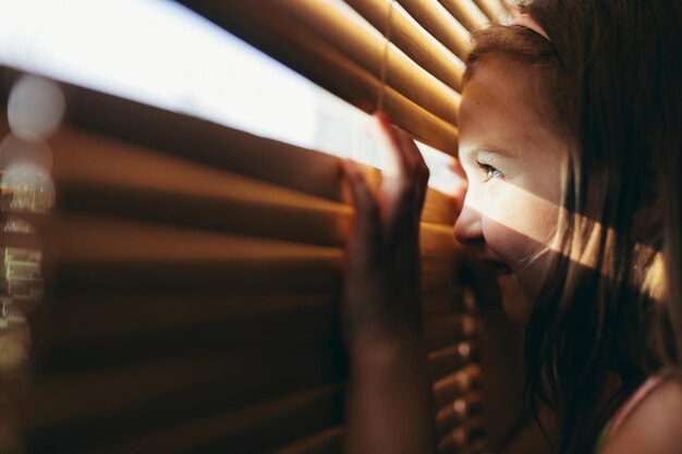 Young girl looking through blinds as if waiting for someone