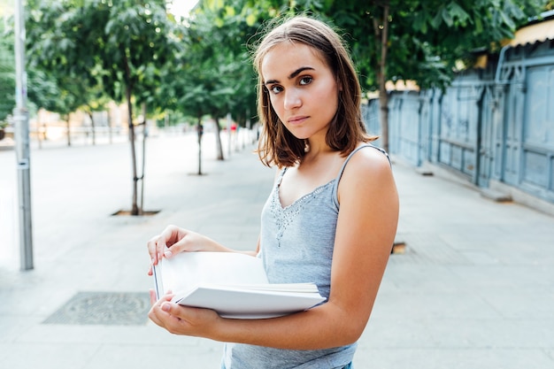 Young girl looks at camera while holding a book on the street