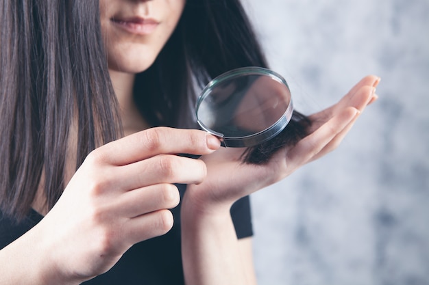 A young girl looks at her hair with a magnifying glass