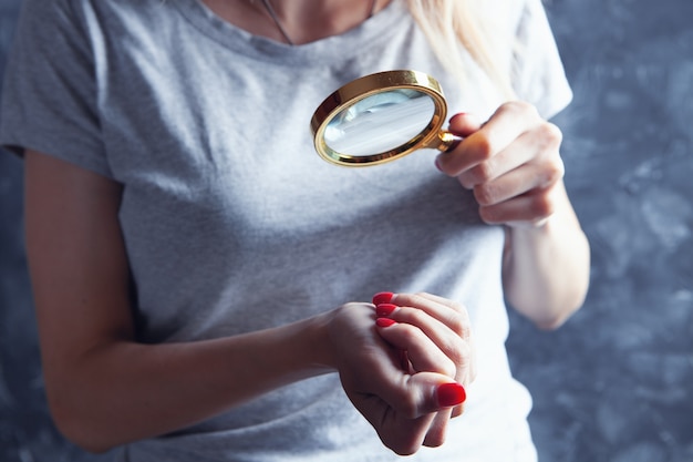 Young girl looks at painted nails with a magnifying glass