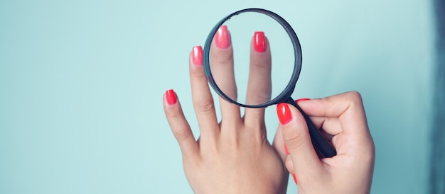 Young girl looks at painted nails with a magnifying glass