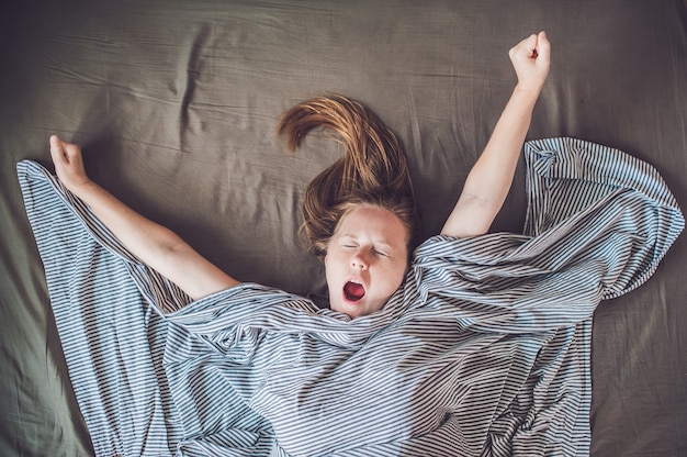 Молодая девушка, лежа в постели под одеялом