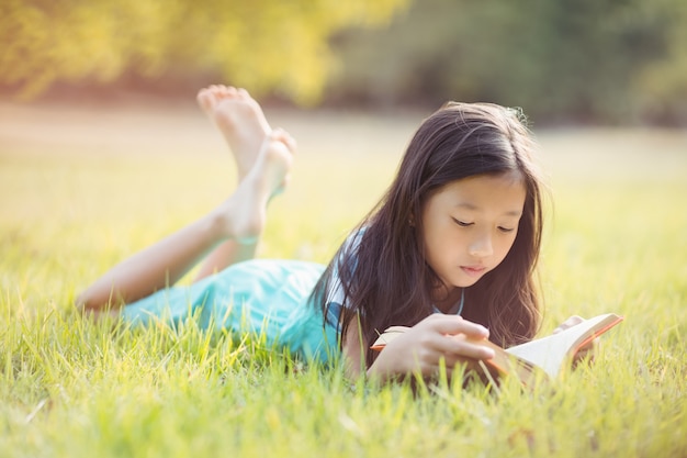 Young girl lying on grass and reading book in park